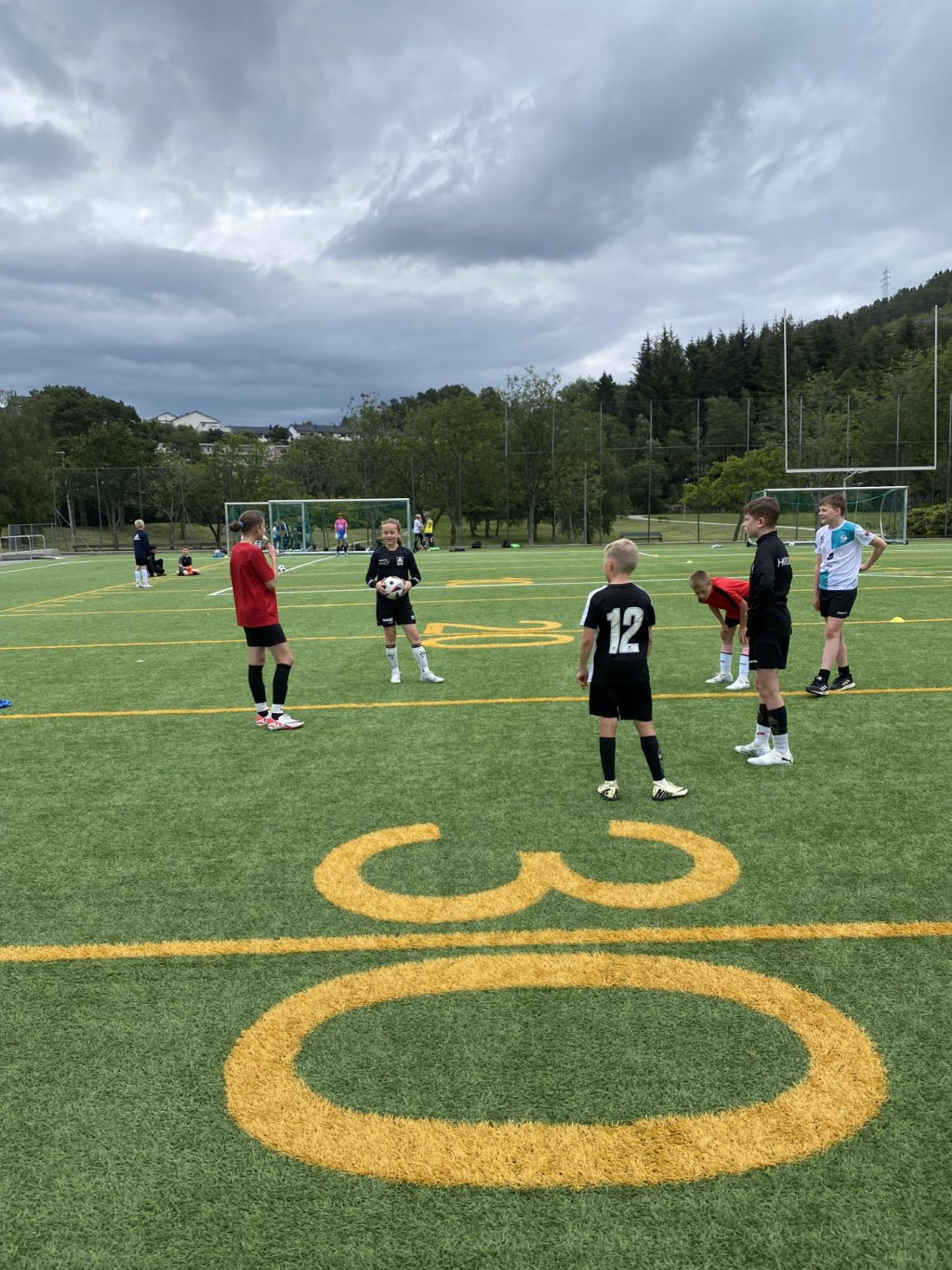 Barn står i ring på fotballbane, et av barna holder en ball